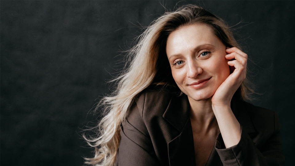 Bohdana Ravliuk - A lady with long, light brown hair, leaning her head on her hand, smiling at the camera. Bohdana Ravliuk - A lady with long, light brown hair, leaning her head on her hand, smiling at the camera.